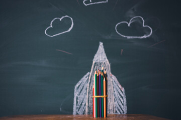 Back to school background with rocket sketch and pencils over chalkboard