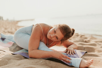 Fototapeta premium Caucasian woman practicing yoga at seashore sandy beach on sunrise. Womens health and wellness. Sports body positive. Real instructor poses