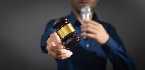 Caucasian auctioneer holding microphone and gavel.