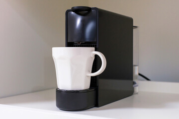 Capsule coffee machine and white mug close-up on a gray background.