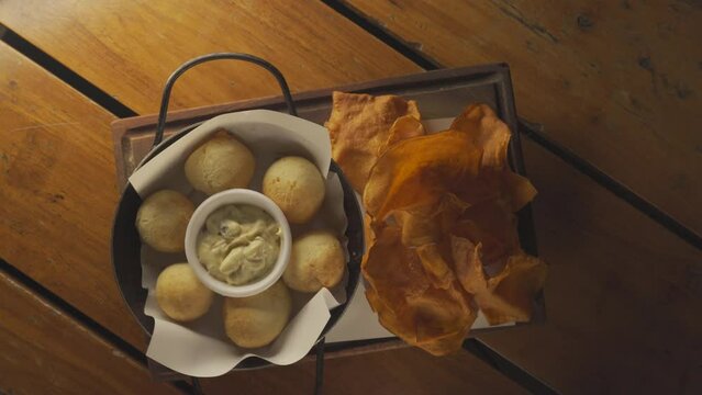 Top down rotating shot of Chipa appetizer snack cheese bites with aioli and potato slices by side. 