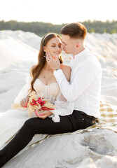Portrait of newlyweds  sitting on sand at sunset.