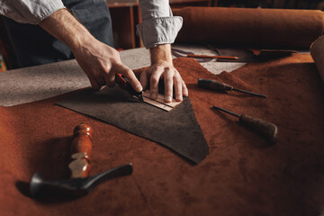 Cobbler Man tailor cuts out blanks for sewing bags or shoes according to pattern made of leather