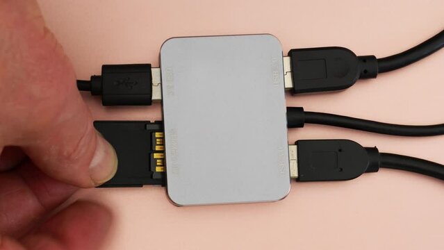 Closeup of a man’s fingers inserting a memory card into one of the inputs of a compact multiport computer adapter / hub. 