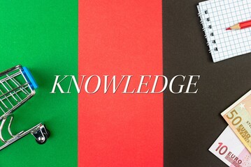 KNOWLEDGE - word (text) and euro money on a table of different colors, a trolley, a basket of grocery notepad and a red pencil. Business concept, buying, selling, supermarket, store (copy space).