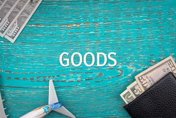 GOODS - word (text) and money dollars on the table in a notepad, wallet and plane. Business...