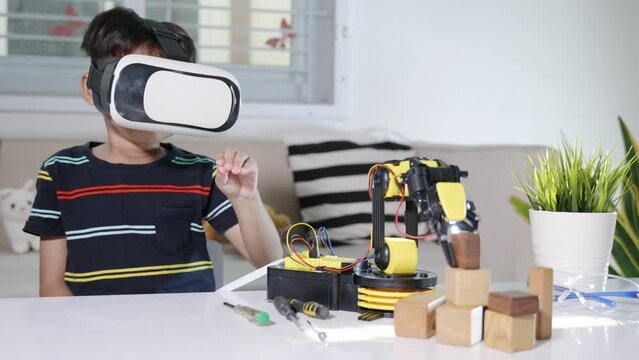 Virtual Reality Simulator. Asian kid boy using VR glasses on robotic arm in workshop, Child learning programer control robot arm with sensors to pick up wood block, Technology education. industry 4.0