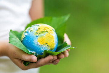 Kid holding small planet in hands against spring or summer green background. Ecology, environment...