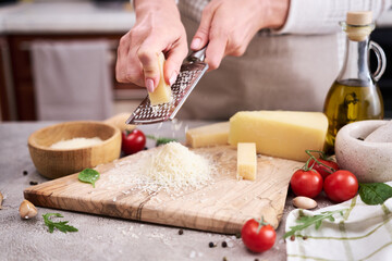 Woman grates Parmesan cheese on a wooden cutting board at domestic kitchen