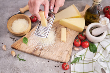 Woman grates Parmesan cheese on a wooden cutting board at domestic kitchen