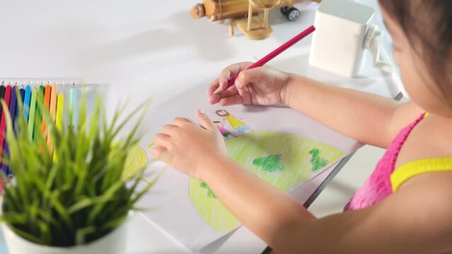 Happy child little girl colorful drawing family standing hold hands on planet earth on paper, Asian cute kid preschooler sit on table smiling she draw picture with pencil at home, earth day concept