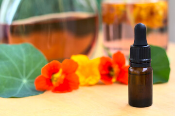 Homemade tincture (elixir) of nasturtium in a dropper. In the distance, a bottle of a ready-made, slightly orange tincture. The whole is decorated with fresh flowers. Shallow depth of field.