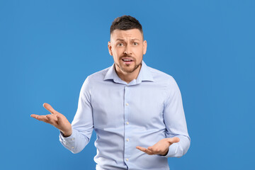 Emotional man in casual outfit on blue background - obrazy, fototapety, plakaty