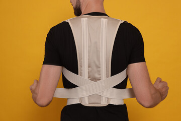 Closeup of man with orthopedic corset on orange background, back view