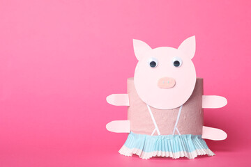 Toy pig made of toilet paper roll on pink background. Space for text
