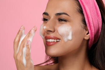 Beautiful woman applying facial cleansing foam on pink background, closeup