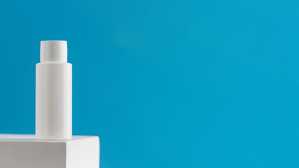 White tube with a cosmetic product on a podium on a blue background. Copy space