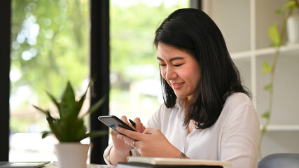 Pleasant asian woman chatting online, typing text message on her smart phone