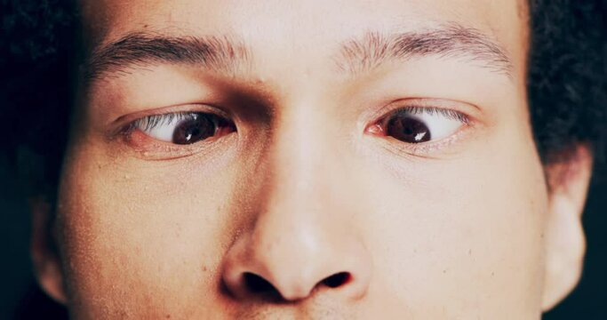 Eyes, vision and comic with a man in studio against a dark background being funny or crazy. Comedy, joke or fun in closeup and zoom on the face and head of a young male looking squint and sideways