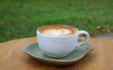 A cup of cappuccino coffee with heart shaped latte art isolated on wooden table