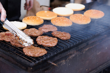 The cook fries meat and heats burger buns on a charcoal grill.