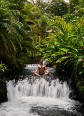 Man meditating sitting in streaming water of Tabacon waterfall, Costa Rica