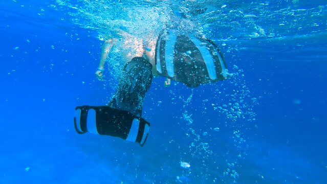 Rear view -woman in fins swimming on the surface of the sea - slow motion. Female snorkeler swims underwater and looking on underwater world