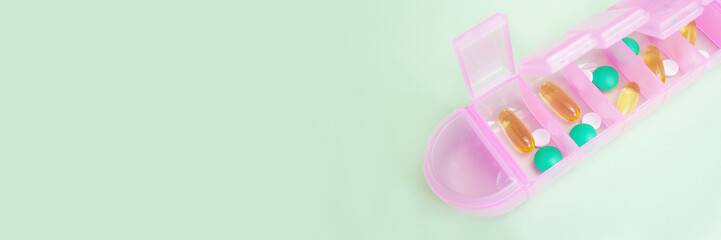 Close-up of pills and capsules in a pink plastic organizer on a light green background. Planning...