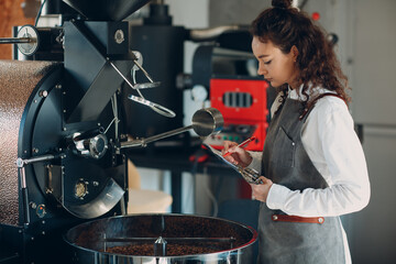 Coffee roaster machine and barista woman with tablet write pen at coffee roasting process.