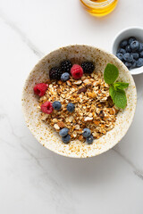 Overhead view of breakfast bowl with granola and berries food on light surface