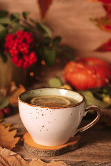 A cup of hot tea with lemon on an autumn background. Autumn and fall vertical postcard. Thanksgiving day or halloween concept.