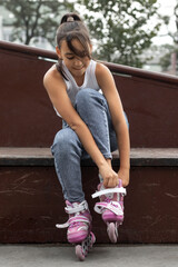 Portrait of a girl putting on inline skates on the playground.