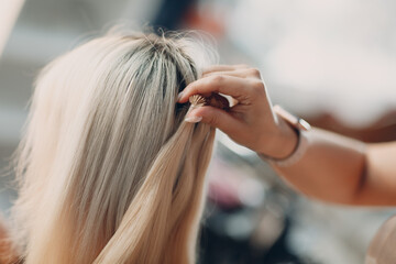 Fototapeta premium Hairdresser female making hair extensions to young woman with blonde hair in beauty salon. Professional hair extension