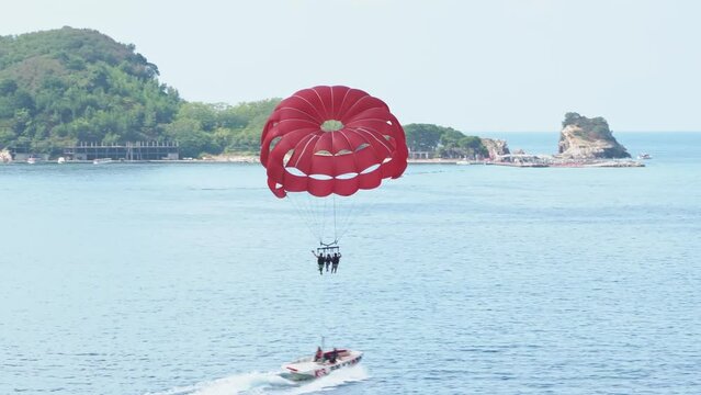 People are flying on a big red parachute attached to a motorboat against the background of the sea. Extreme leisure activities in the resort towns of detom. Parasailing.