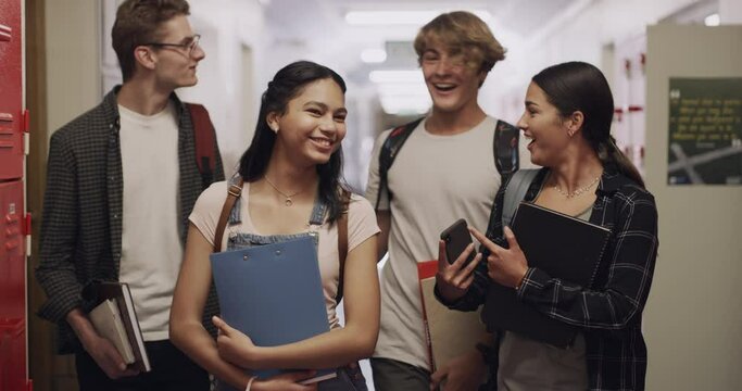 Students, communication and friends with a phone talking and walking in a high school hall. Happy student group smile looking at social media, web and online content in a conversation going to class