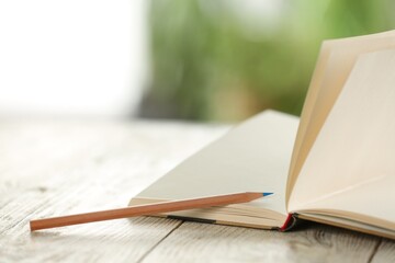 Closeup view of open notebook with pencil on white wooden table against blurred background