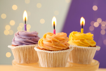 Tasty birthday cupcakes with candles on stand against blurred lights, closeup
