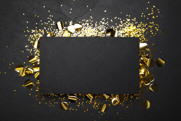 Slate board and confetti on black background, top view. Space for text
