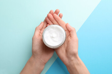 Woman holding jar of hand cream on color background, top view