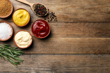 Flat lay composition with ketchup, mustard, mayonnaise and ingredients on wooden table, space for...