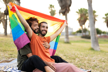 Fototapeta na wymiar Gay couple embracing and showing their love with rainbow flag. LGBT community.