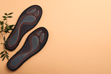 Pair of orthopedic insoles and leaves on pale orange background, top view. Space for text