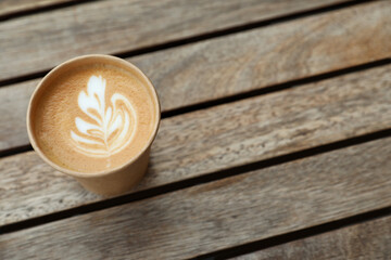 Takeaway paper cup with coffee on wooden table, above view. Space for text