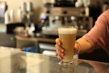 Barista putting glass with delicious coffee on countertop in cafe, space for text
