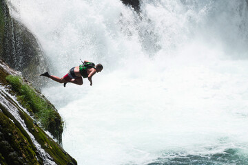 waterfall extreme brave man as superhero running jump and dive from the rock into the wild river...