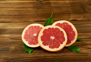 Fototapeta na wymiar Grapefruit slices on a wooden background with green leaves. Beautiful photo wallpaper. 