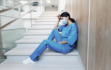 Tired female doctor after hard working day in medical clinic sitting on steps in hospital with eyes closed wearing medical mask. Pandemia coronavirus