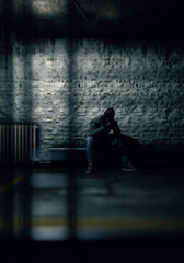 Man in hoodie sits on bench in dark prison. 3D render.