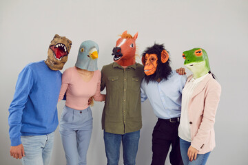 Cheerful young people in various original masks in form of animal heads hugging looking at camera....