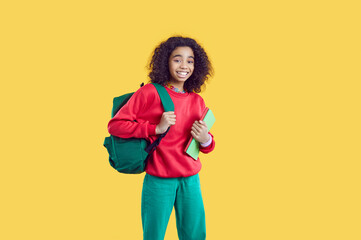Happy school child. Cheerful kid with books and backpack. African American student girl in modern...